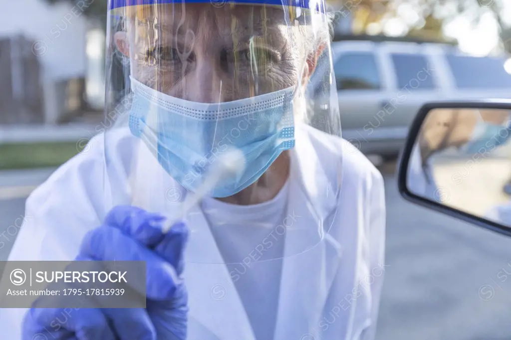 Female medical staff in protective clothing approaching car with coronavirus swab test