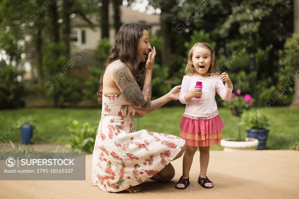 Mother and toddler daughter blowing bubbles in garden