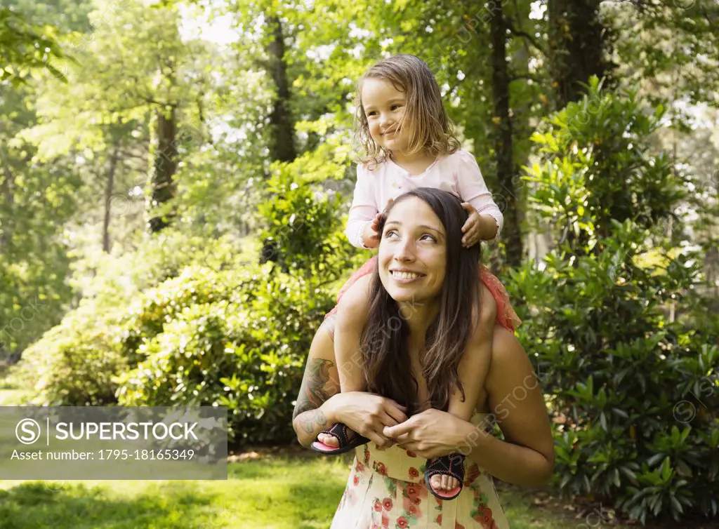 Mother giving toddler daughter a shoulder carry in park