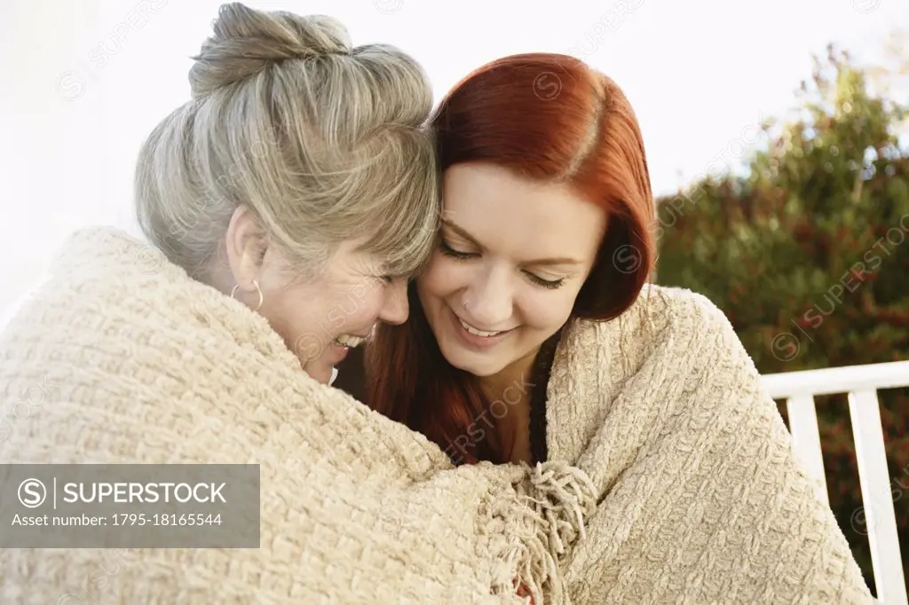 Senior woman and adult daughter face to face wrapped in a blanket on porch