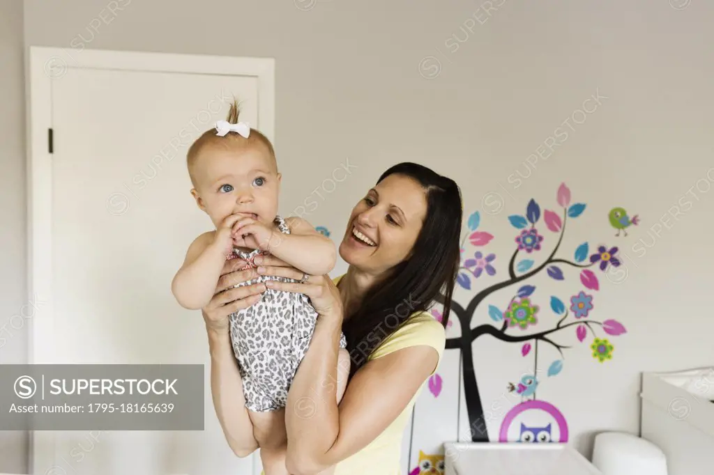 Happy mid adult mother holding up baby daughter