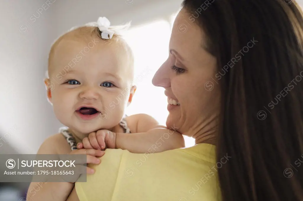 Over the shoulder portrait view of happy baby girl and mid adult mother