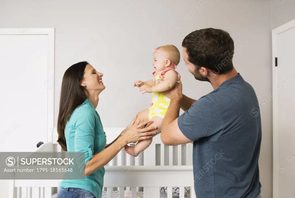 Mid adult couple holding up baby daughter in nursery