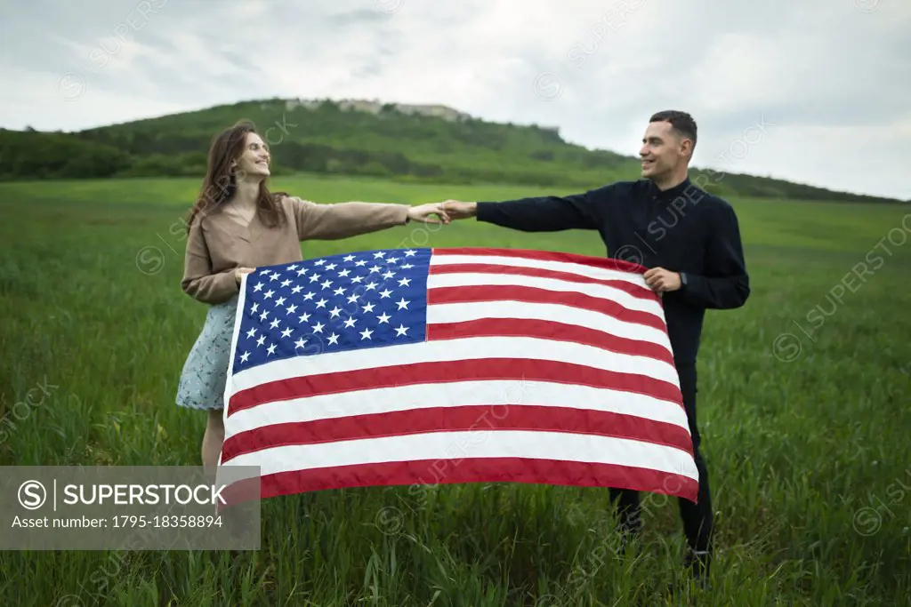 Young couple holding American flag in wheat field