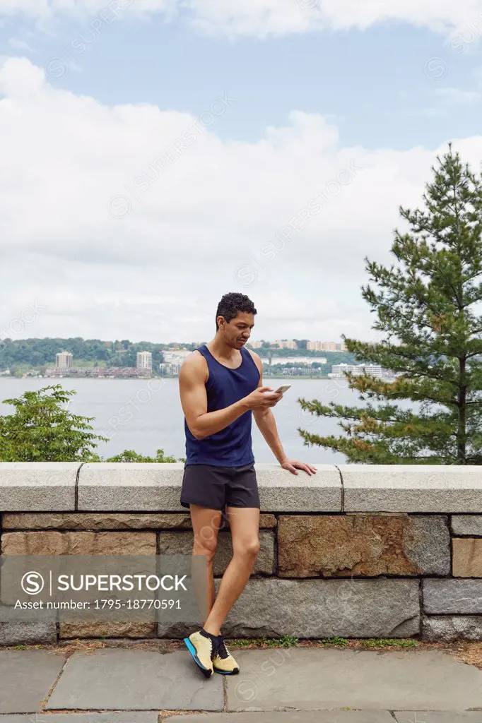 USA, New York, New York City, Man in sports clothing looking at smart phone at wall in park