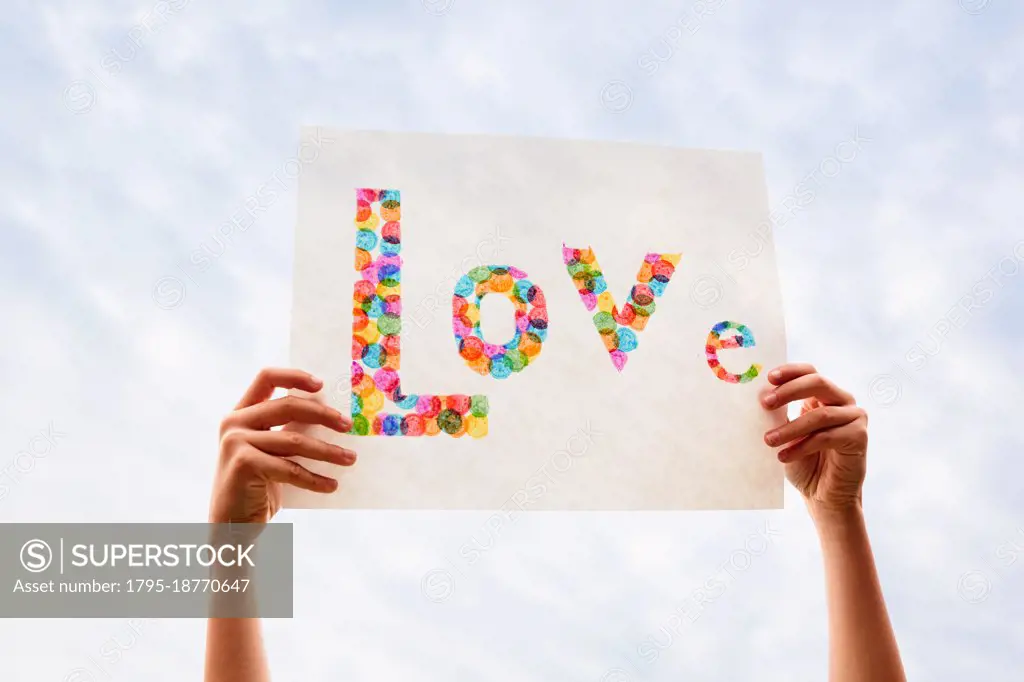 Hand of boy (8-9) holding colorful Love sign against sky