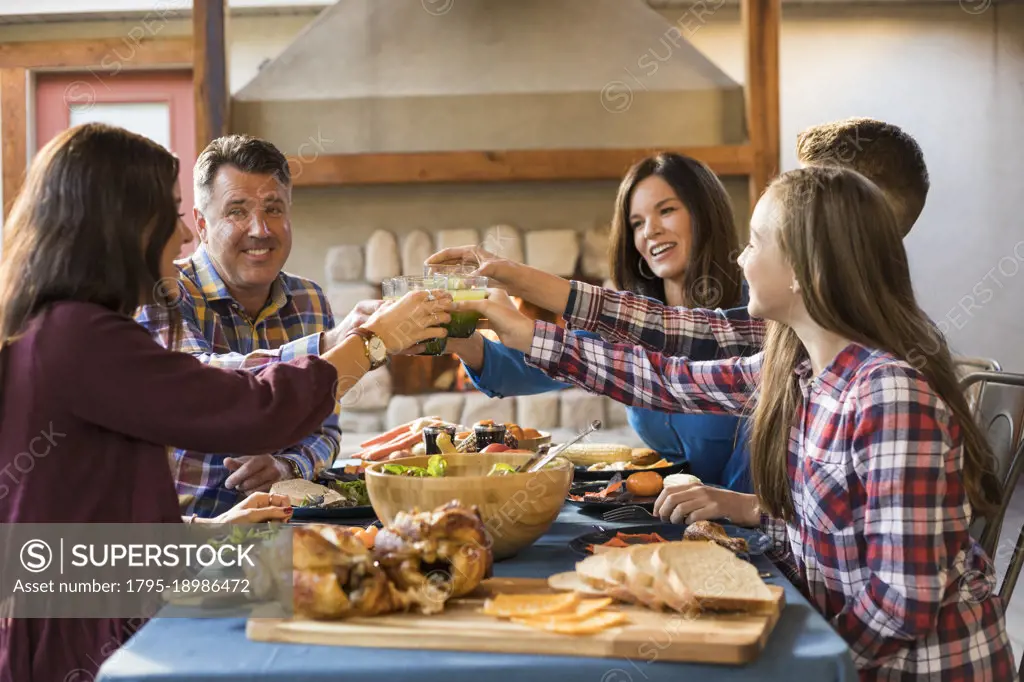 Family with children (10-11, 12-13, 16-17) raising toast with orange juice