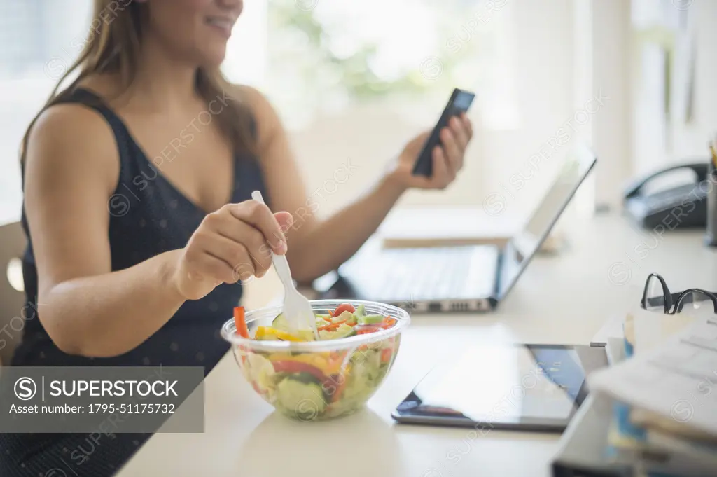 Woman working in home office and eating salad