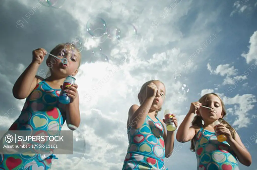 Three young sisters blowing bubbles