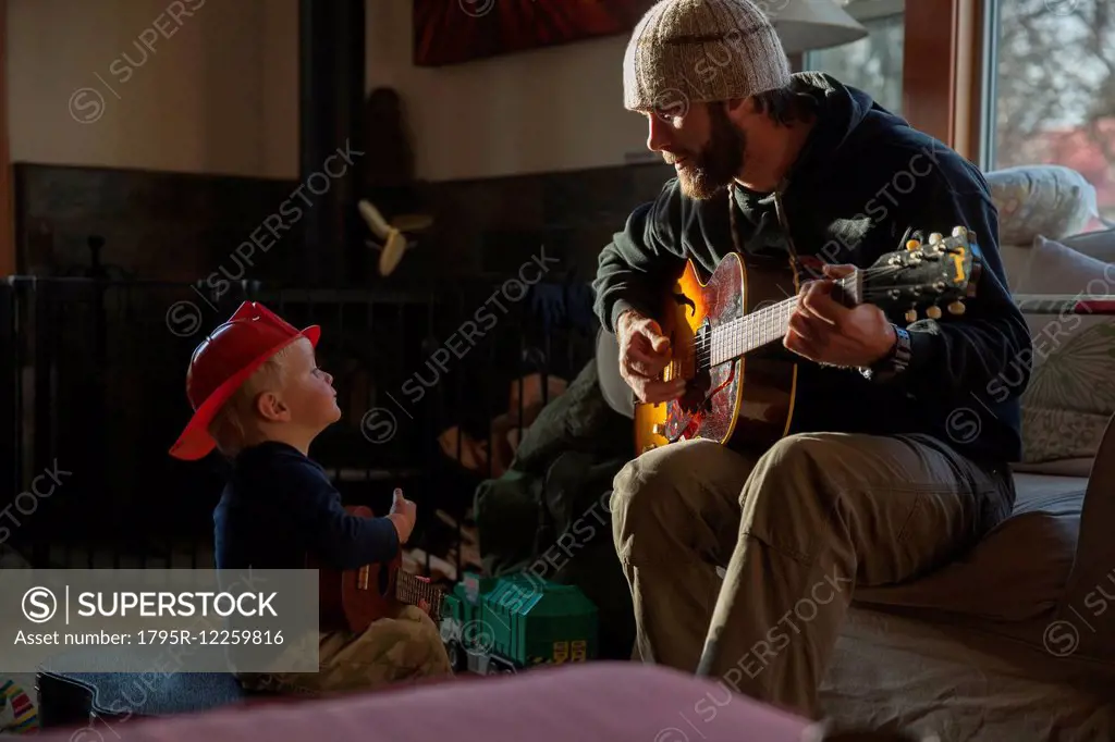 Boy (4-5) listening his dad playing guitar