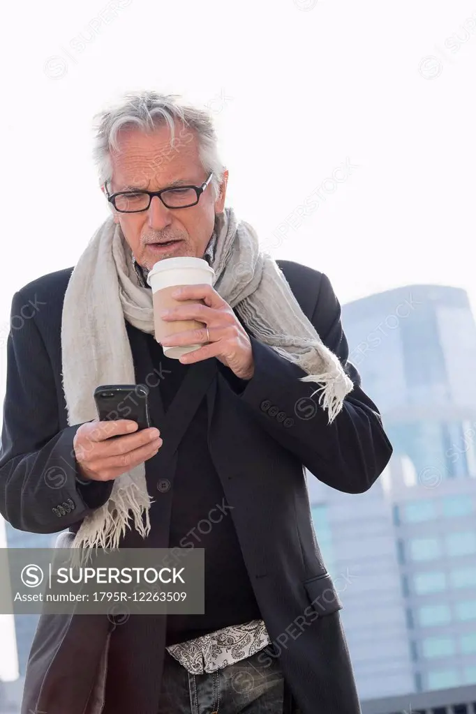 Man in street drinking coffee using smartphone