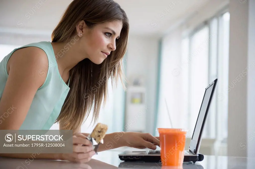 Young woman eating snack while working with laptop
