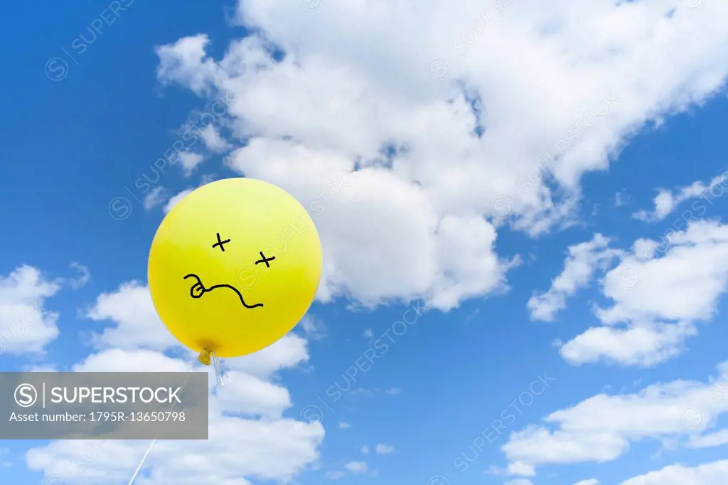 Yellow balloon with drawn face against blue sky