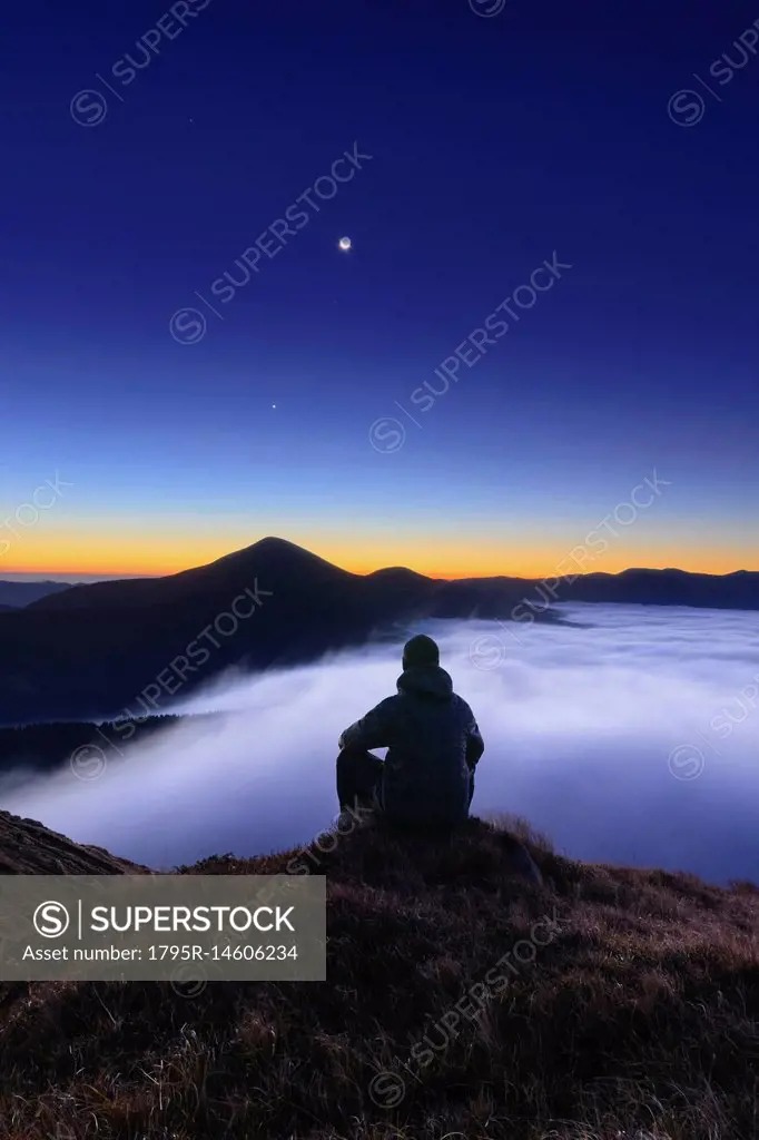 Ukraine, Zakarpattia region, Rakhiv district, Carpathians, Chornohora, Tourist sitting on mountain meadow at dusk