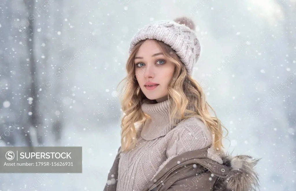 Portrait of young woman in woolly hat under snowfall