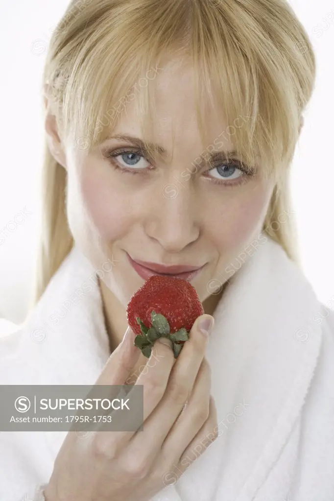 Woman in bathrobe eating strawberry