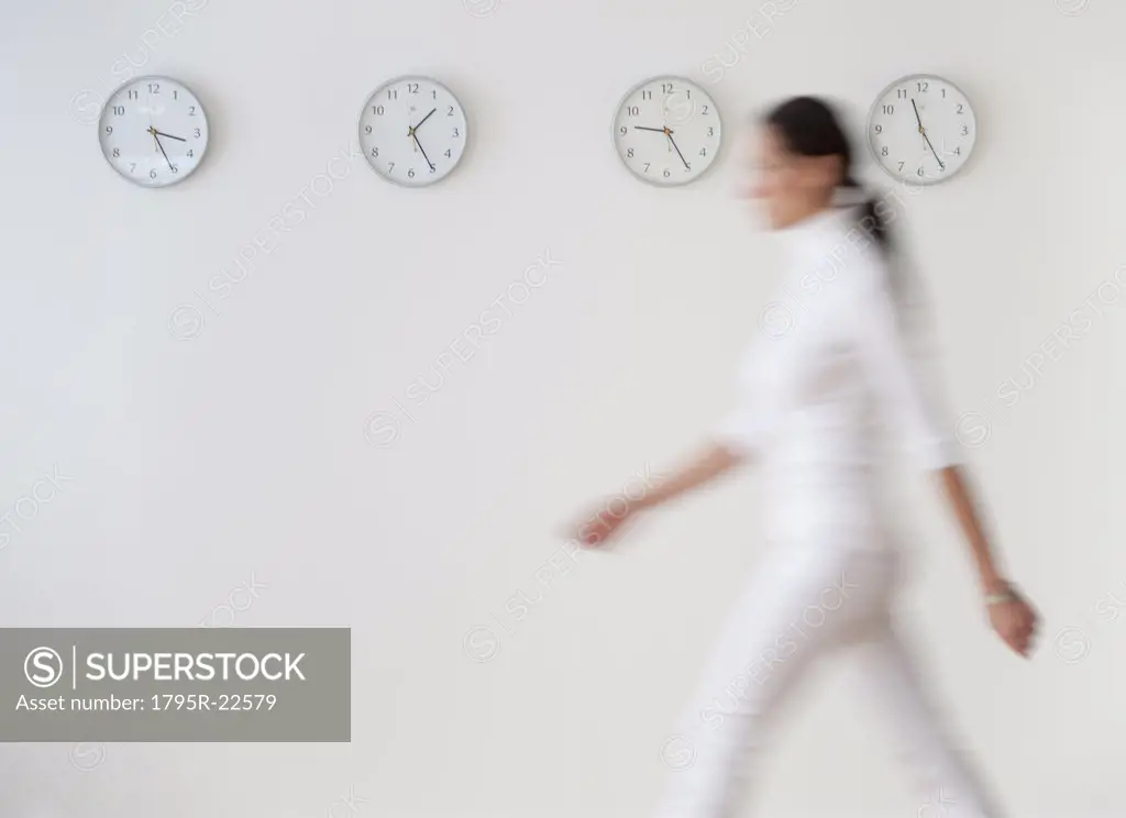 Business woman walking along wall with clocks, blurred motion