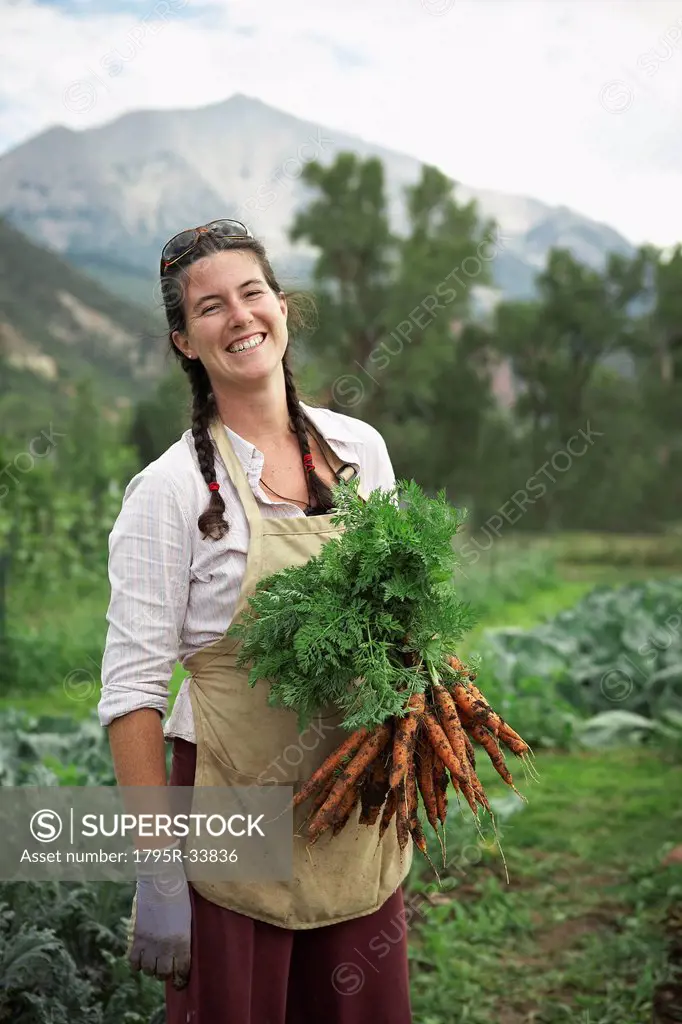 Portrait of woman holding carrots in field