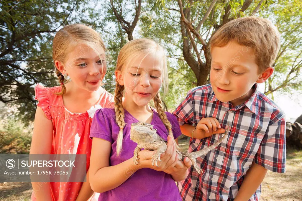 Three kids 4_5, 6_7 excited to be looking at lizard being held by child in the middle