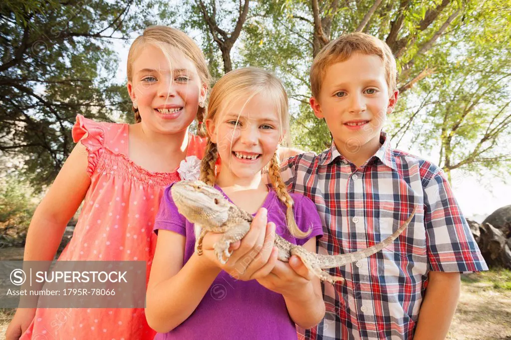 Three kids 4_5, 6_7 excited to be looking at lizard being held by child in the middle