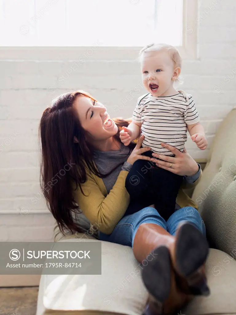 Mother and daughter (12-17 months) playing on sofa, Laughing and having fun