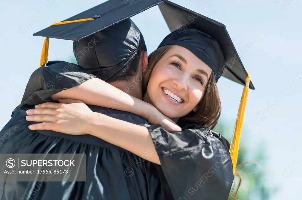 Female and male students embracing on graduation ceremony