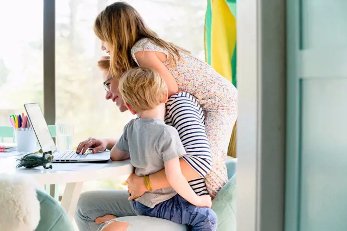 Children (4-5, 6-7) climbing on their mother while she works from home