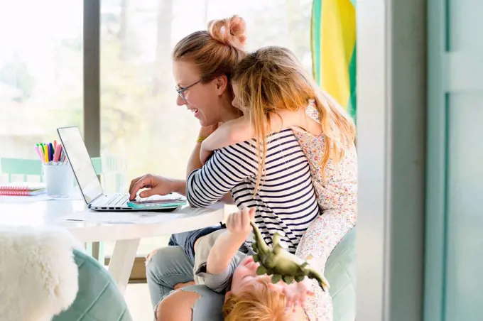 Children (4-5, 6-7) climbing on their mother while she works from home