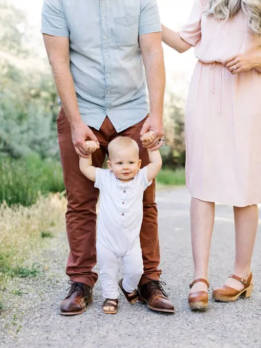 Parents assisting baby son learning to walk outdoors