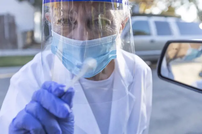 Female medical staff in protective clothing approaching car with coronavirus swab test