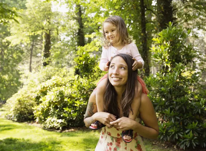 Mother giving toddler daughter a shoulder carry in park