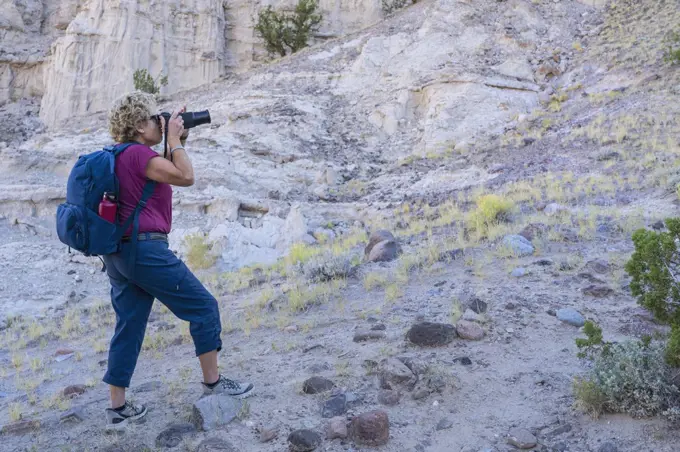 USA, New Mexico, Abiquiu, Woman with backpack photographing rocky landscape