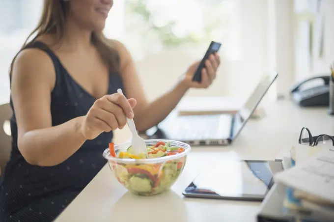 Woman working in home office and eating salad