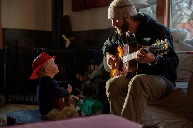 Boy (4-5) listening his dad playing guitar