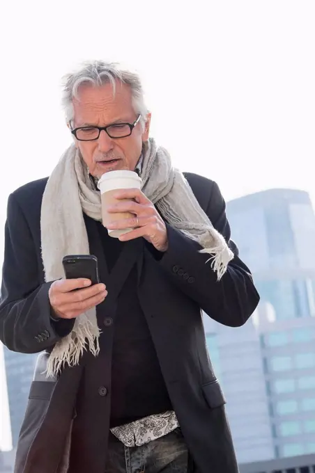 Man in street drinking coffee using smartphone