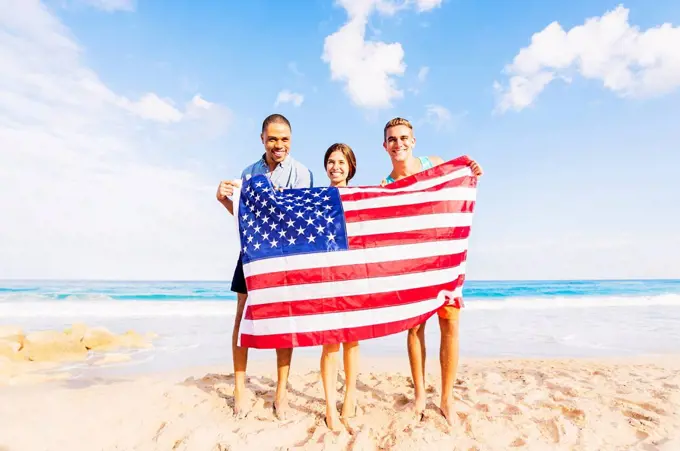 Young people holding American flag on beach