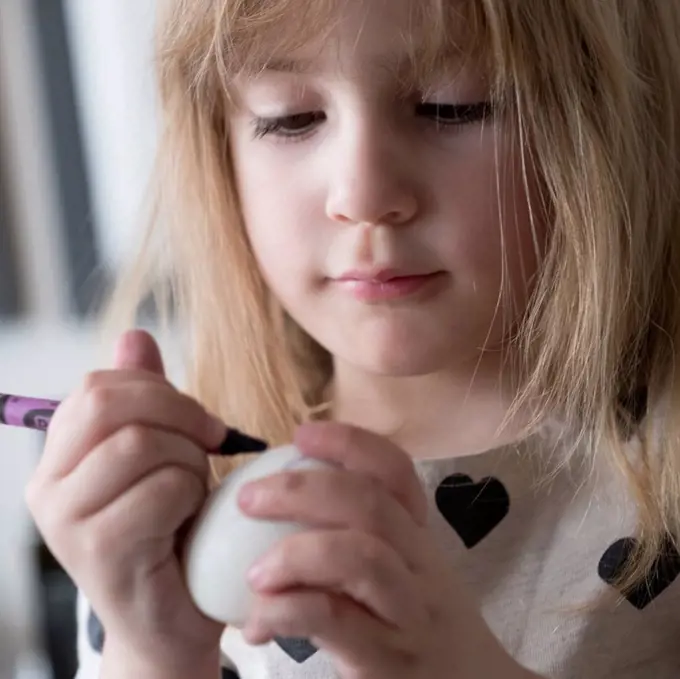 Girl (4-5) making colored Easter eggs