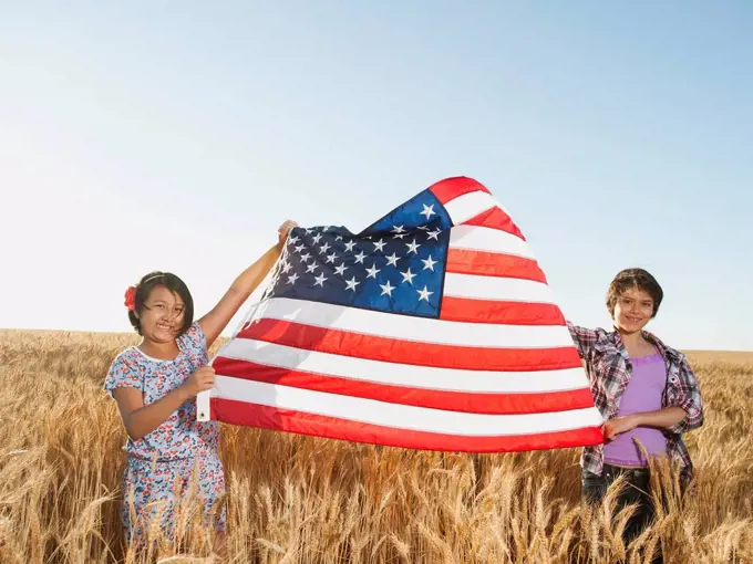 Girls 10_11, 12_13 holding american flag in wheat field