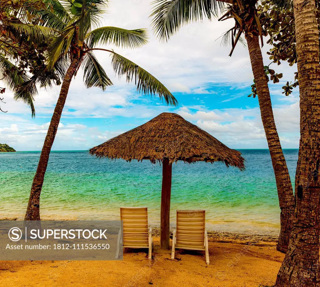 Two chairs under a thatched umbrella on the beach looking out to the turquoise ocean water; Malolo Island, Fiji