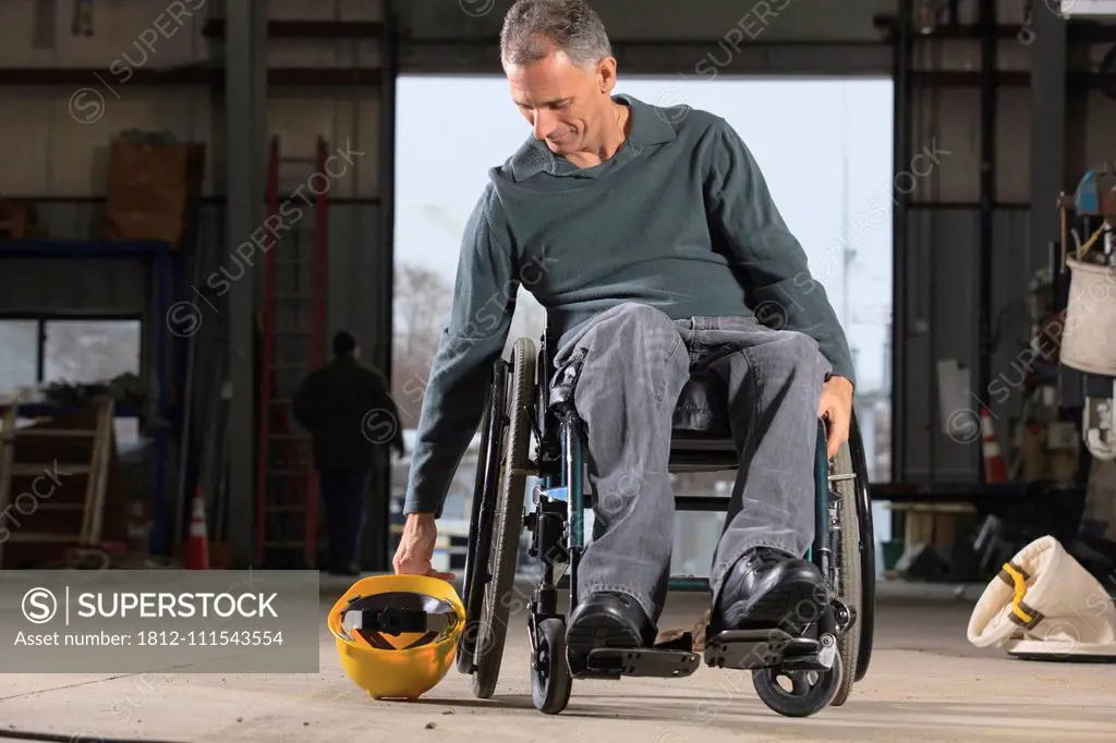 Engineer with spinal cord injury picking up his hard hat in the maintenance garage