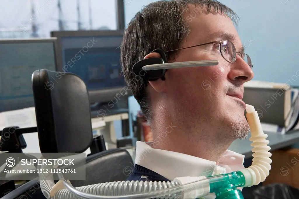 Businessman with Duchenne muscular dystrophy in a motorized wheelchair using a breathing ventilator and a hearing device in an office