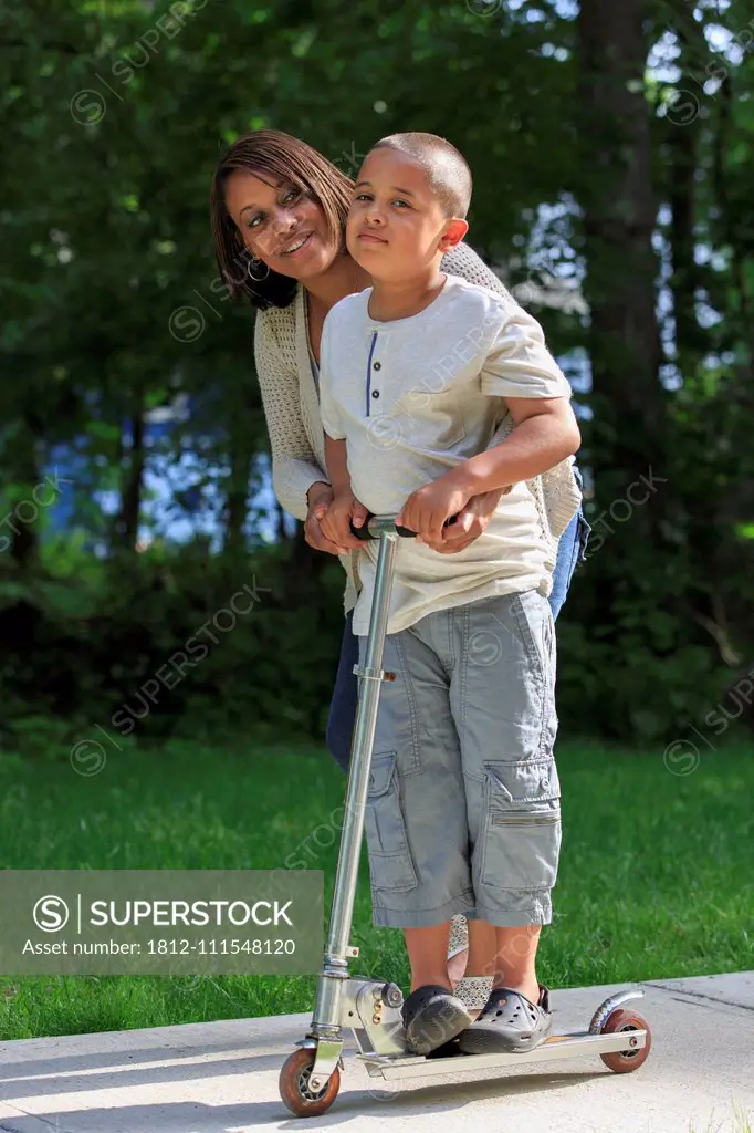 Hispanic boy with Autism playing on a push scooter with his mother in park