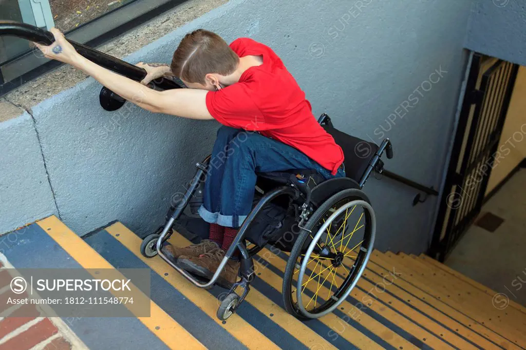 Trendy man with a spinal cord injury in wheelchair going down subway stairs backwards