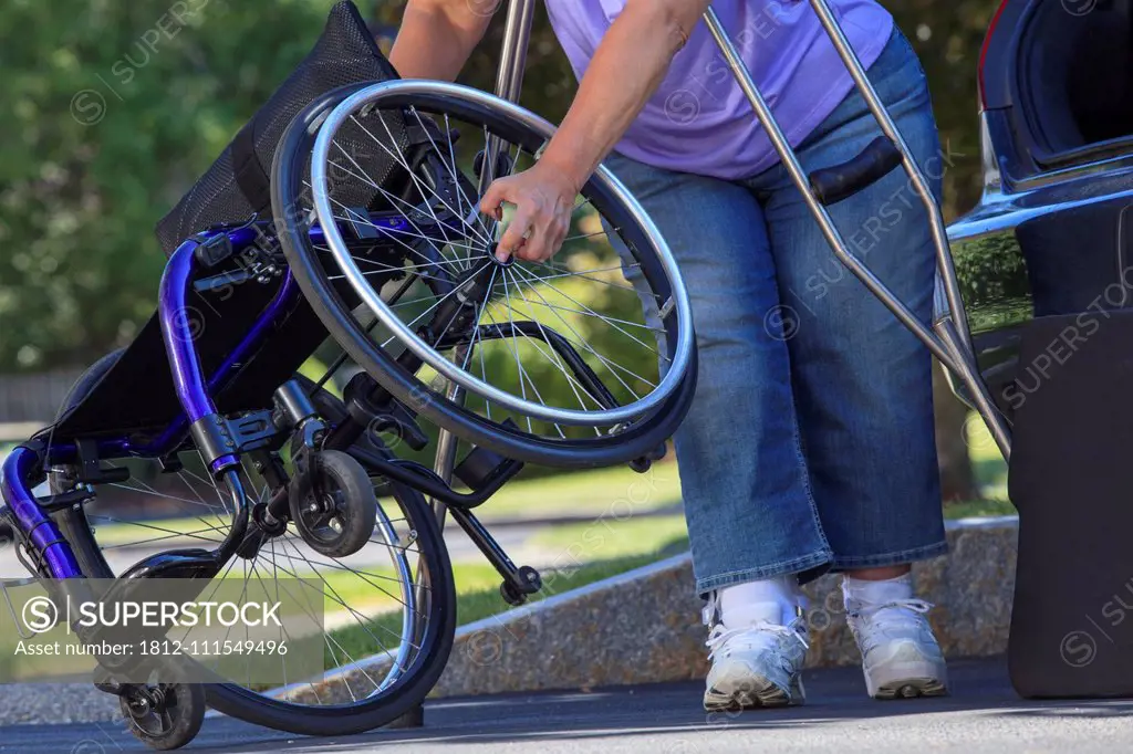 Woman with Spina Bifida using crutches to take wheelchair apart for traveling in the car