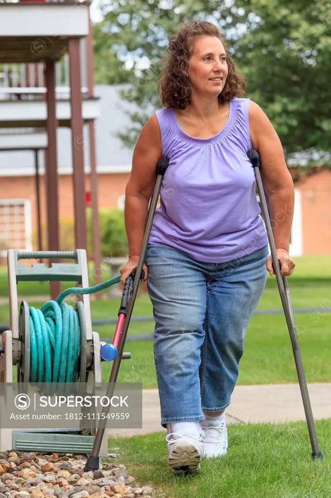 Woman with Spina Bifida walking with crutches and pulling garden hose