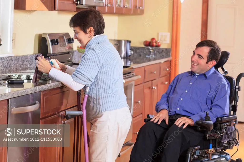 Woman with Cerebral Palsy using crutches and working in her kitchen while talking to her husband with Cerebral Palsy