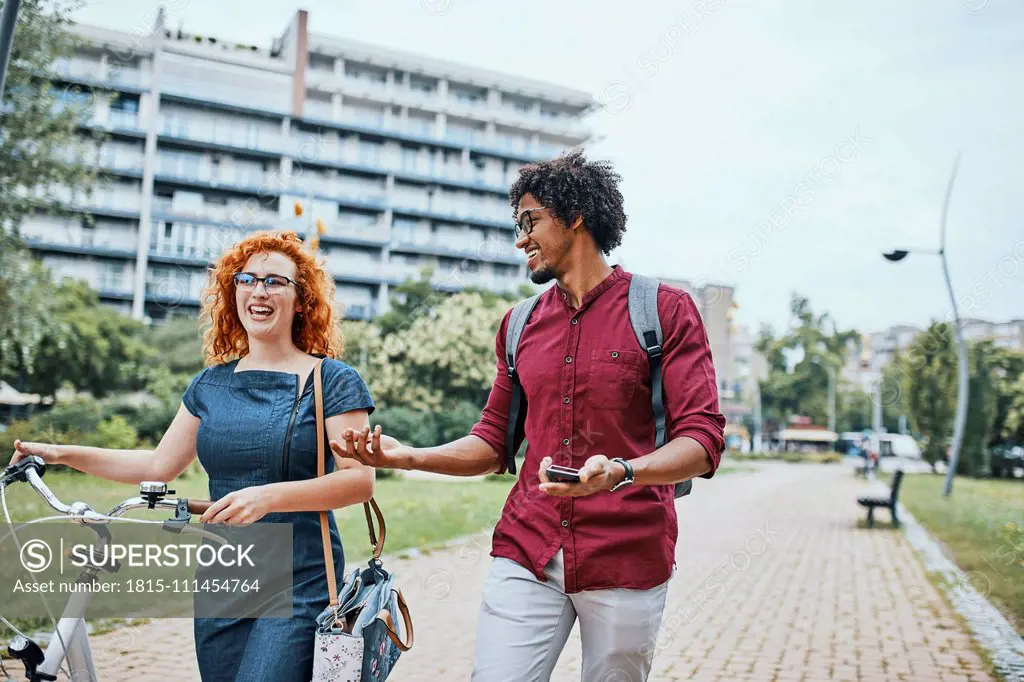 Friends walking in park, talking, woman pushing bicycle