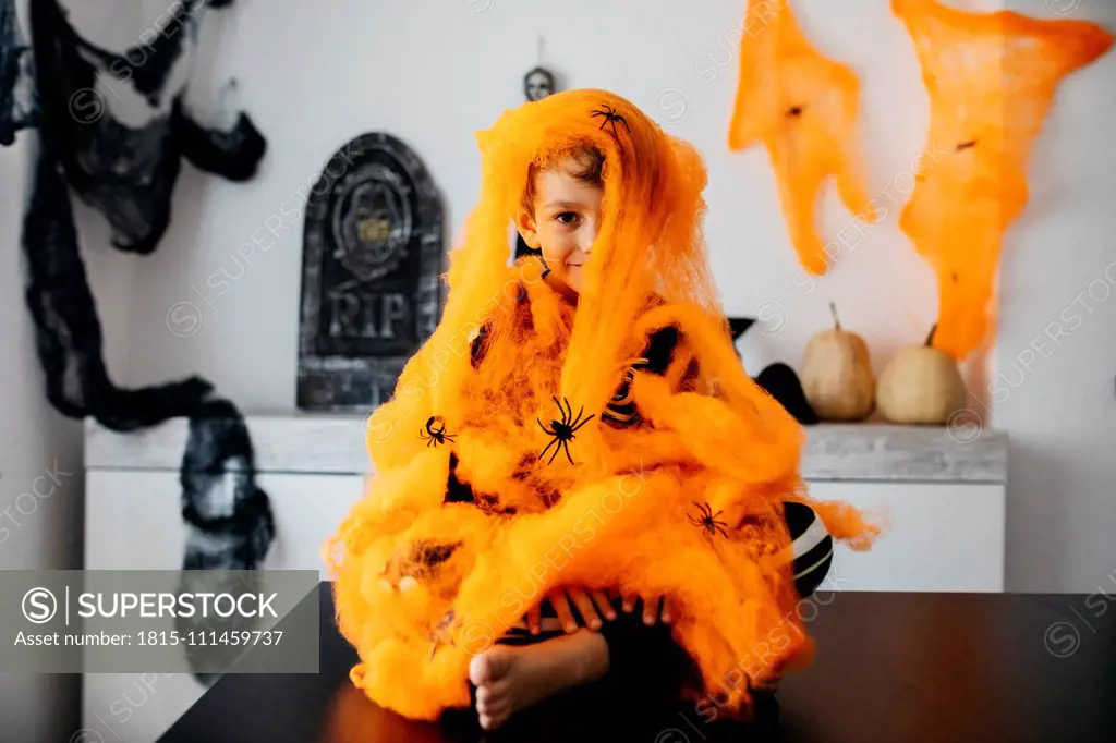 Little boy wrapped in orange spider web at Halloween