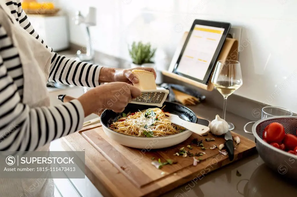 Close-up of woman with tablet cooking pasta dish in kitchen at home