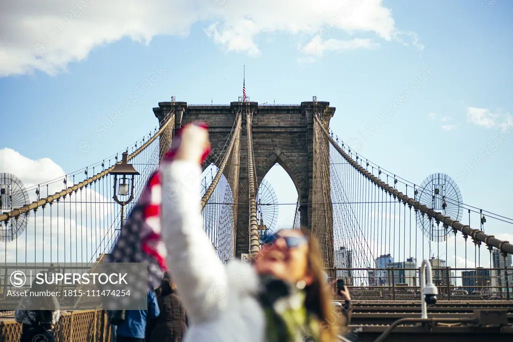 Woman standing on Brooklyn Bridge holding the American flag, New York, United States